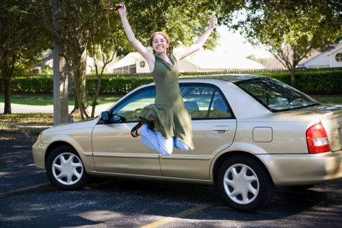 Teen girl with new car jumps for joy.